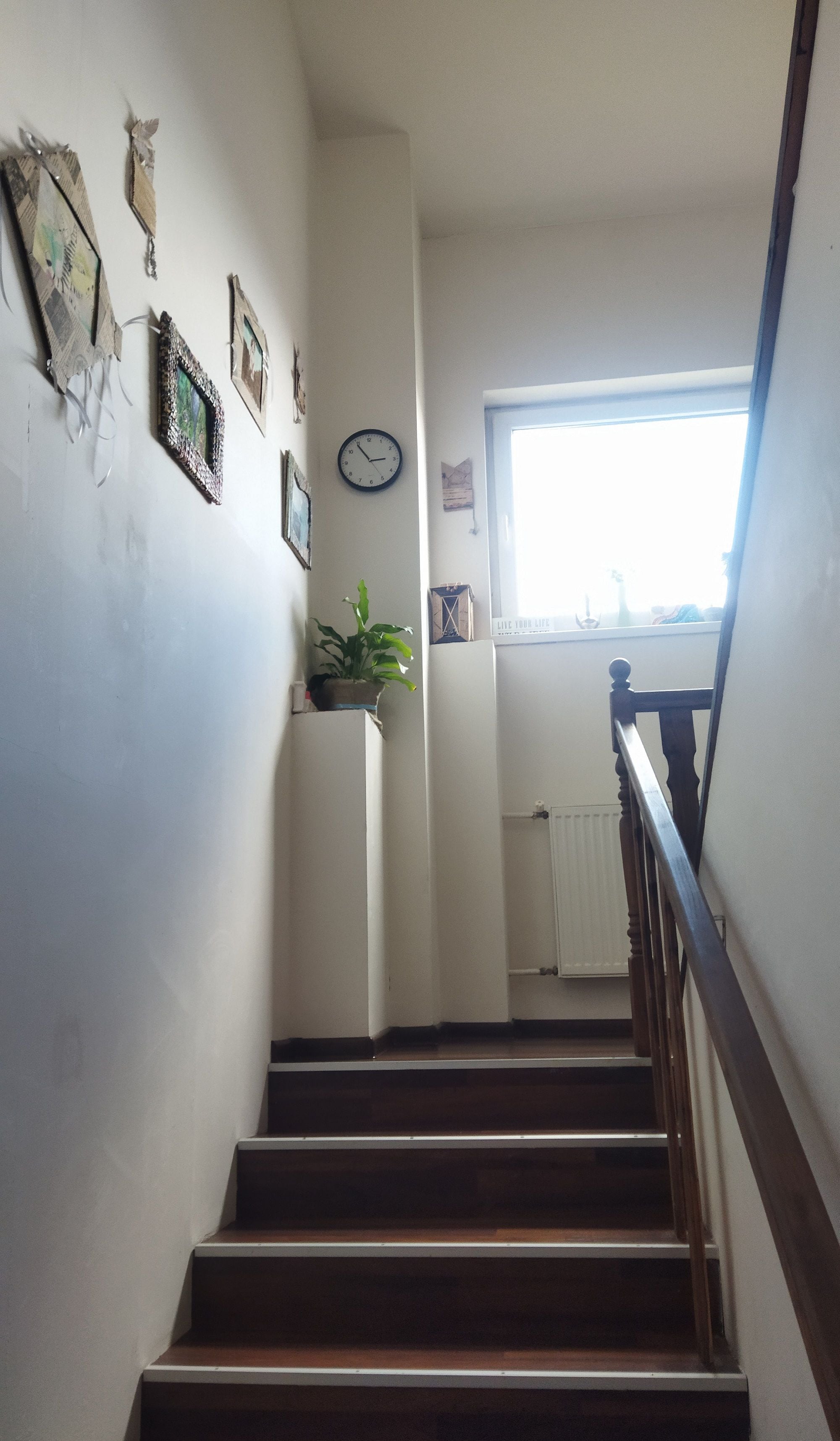 A staircase with wooden steps leading to a landing with a clock and a potted plant.