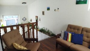 A living room with a wooden staircase, a sofa, and a chair. There are several potted plants on the staircase and a window with a view of the outside. - Lucky Cat  (Nova Lesna)