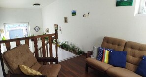 A living room with a wooden staircase, a sofa, and a chair. There are several potted plants on the staircase and a window with a view of the outside. - Lucky Cat  (Nova Lesna)