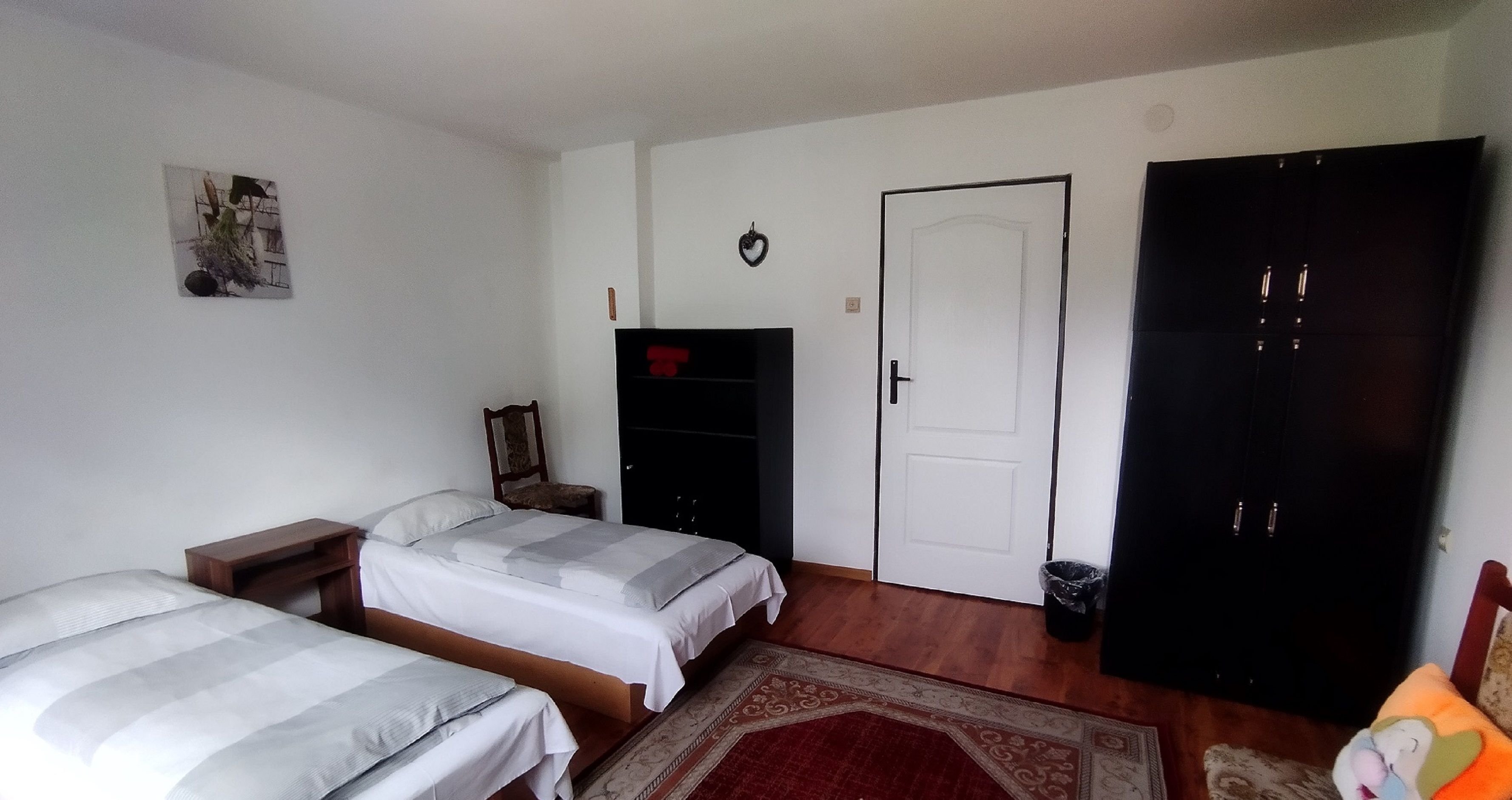 A bedroom with two beds, a wardrobe, a chair, a door, and a small trash bin.