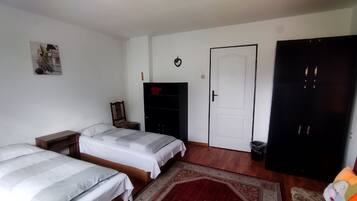 A bedroom with two beds, a wardrobe, a chair, a door, and a small trash bin.