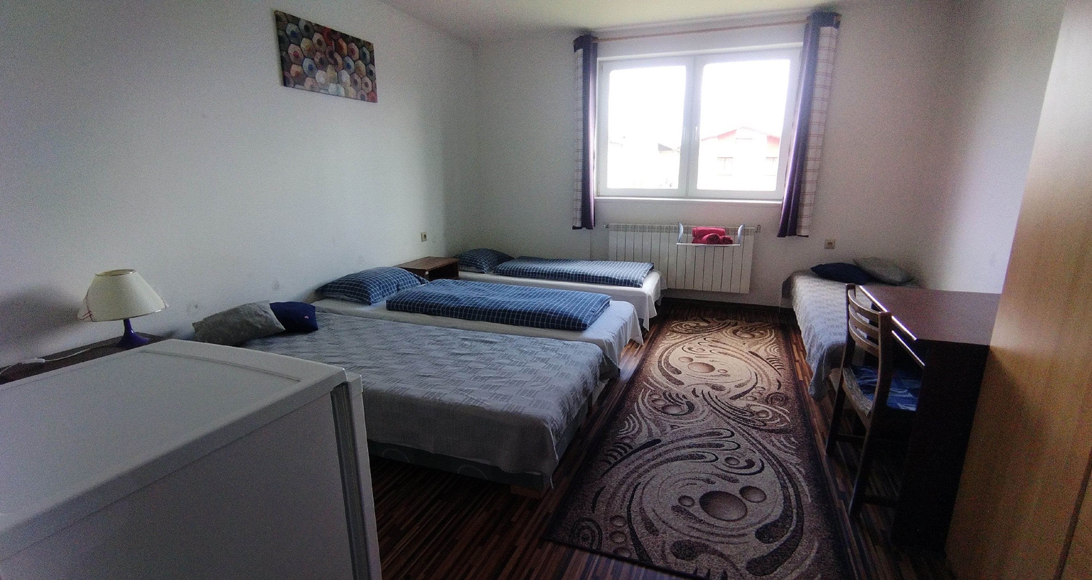 Habitació petita i ben neta amb dos llits individuals, un escriptori, una làmpada i una finestra amb cortines.