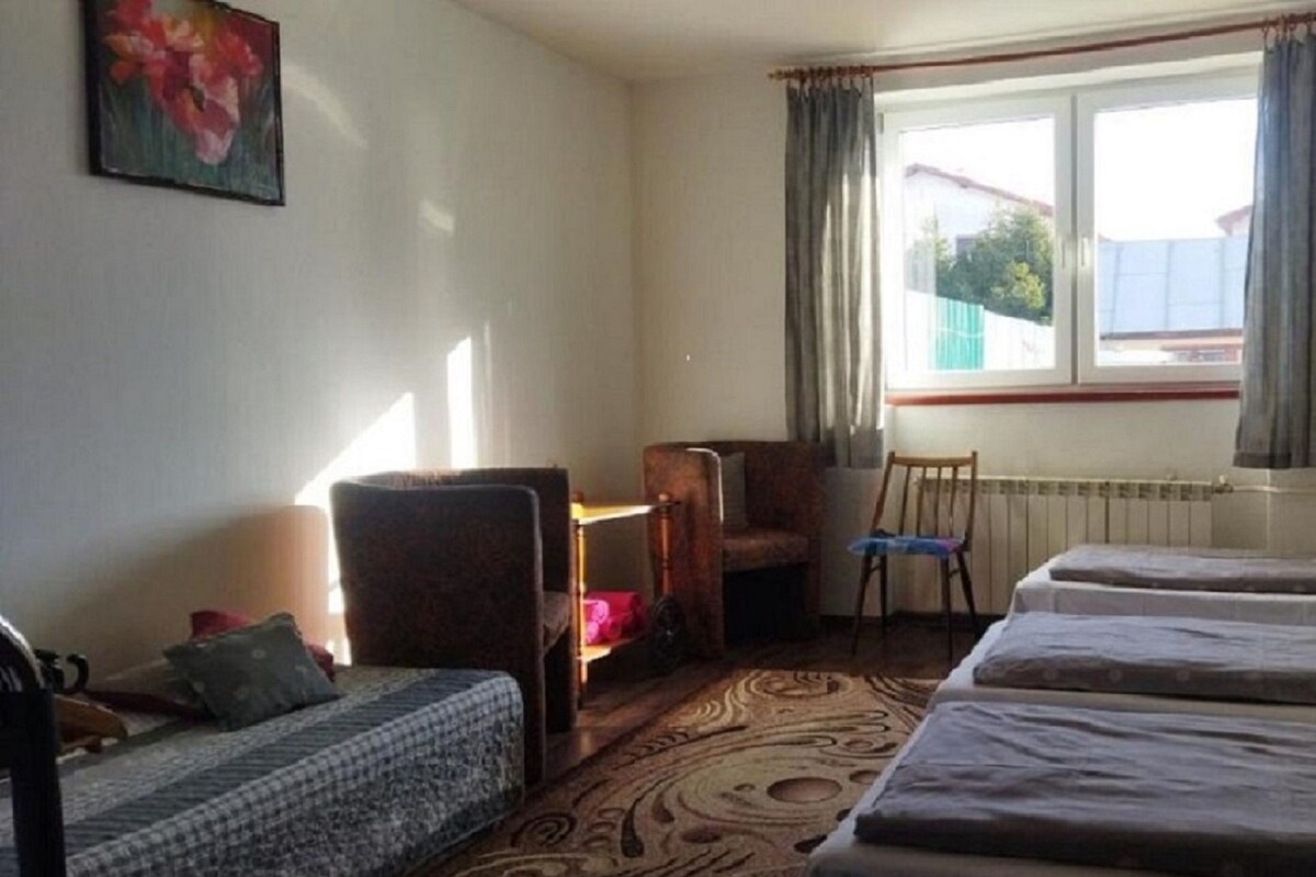 A hotel room with two single beds, a sofa, a chair, a small table, and a window with curtains.