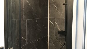 A shower enclosure with dark marble tiles and a black showerhead. - Maisont3 Duplex Avec Cour Privée à 400 Plage (Angoulins)
