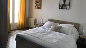 A bedroom with a large bed, a bedside table with a lamp, a radiator, and artwork on the wall. - Maisont3 Duplex Avec Cour Privée à 400 Plage (Angoulins)
