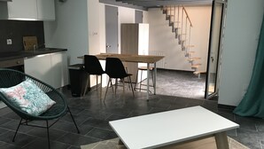 A modern kitchen with white cabinets, a dining area with a wooden table and black chairs, and a staircase leading to another level. - Maisont3 Duplex Avec Cour Privée à 400 Plage (Angoulins)