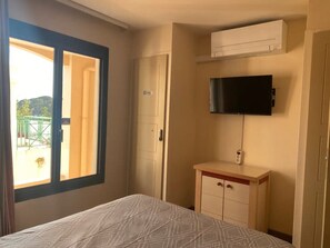 Quarto de hotel com uma cama, uma televisão fixada na parede, um pequeno armário e uma porta deslizante para uma varanda.