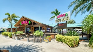 Um restaurante com uma placa indicando 'Grills Tiki Bar' e uma área de estar ao ar livre coberta.