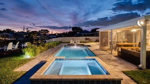 Piscina retangular com borda azulejada, rodeada por um espaço de terraço com mobiliário de exterior e cerca branca.