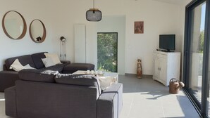 Een moderne woonkamer met een modulaire bank, een flatscreen televisie en een groot raam met uitzicht op groen.