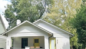 Ein einstöckiges Haus mit Veranda, einer gelben Tür und der Hausnummer 3B an der Seite.