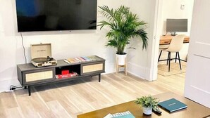 Ein modernes Wohnzimmer mit Flachbildfernseher, Couchtisch mit Büchern, Topfpflanze und minimalistischem Design.