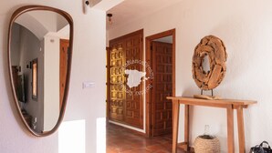 Un couloir avec une porte en bois, un miroir, une table en bois ornée d’un objet décoratif et un panier tressé.
