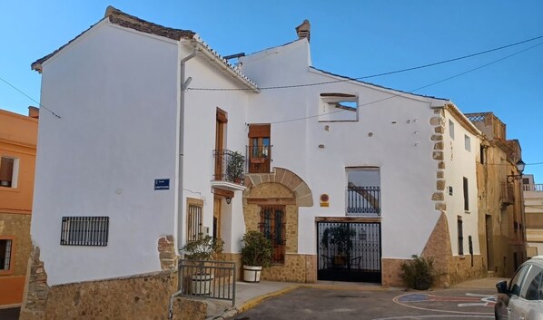 Un edificio blanco con base de piedra, un balcón y una entrada protegida por una reja.