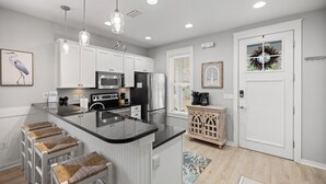 A modern kitchen with white cabinets, a central island with stools, stainless steel appliances, and pendant lighting.