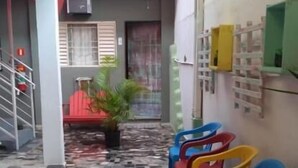 Un pasillo con piso de baldosas, sillas de plástico de colores, una escalera y un balcón con barandilla.