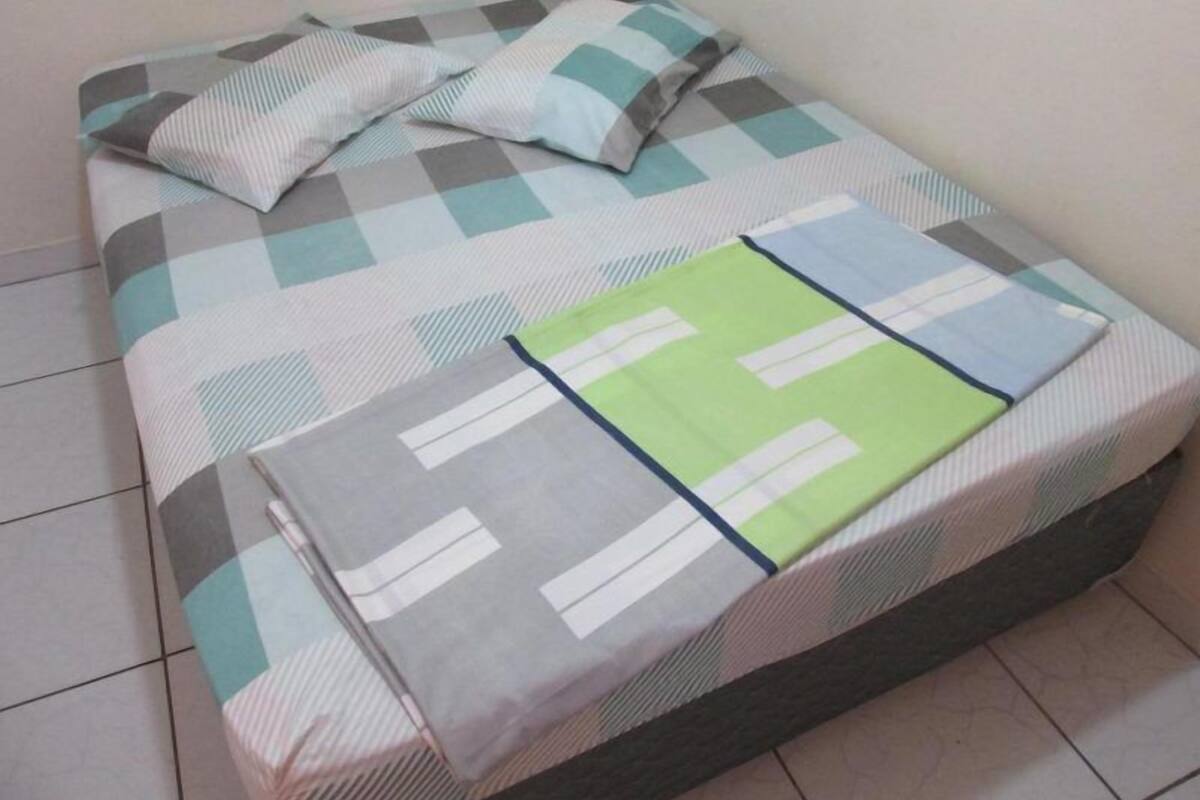 A bed with a checkered bedspread and pillows, a green blanket, and a grey blanket.