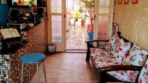 Una habitación acogedora con pared de azulejos, un sofá con cojines estampados, una zona de bar con televisor y una puerta que da a un patio exterior.
