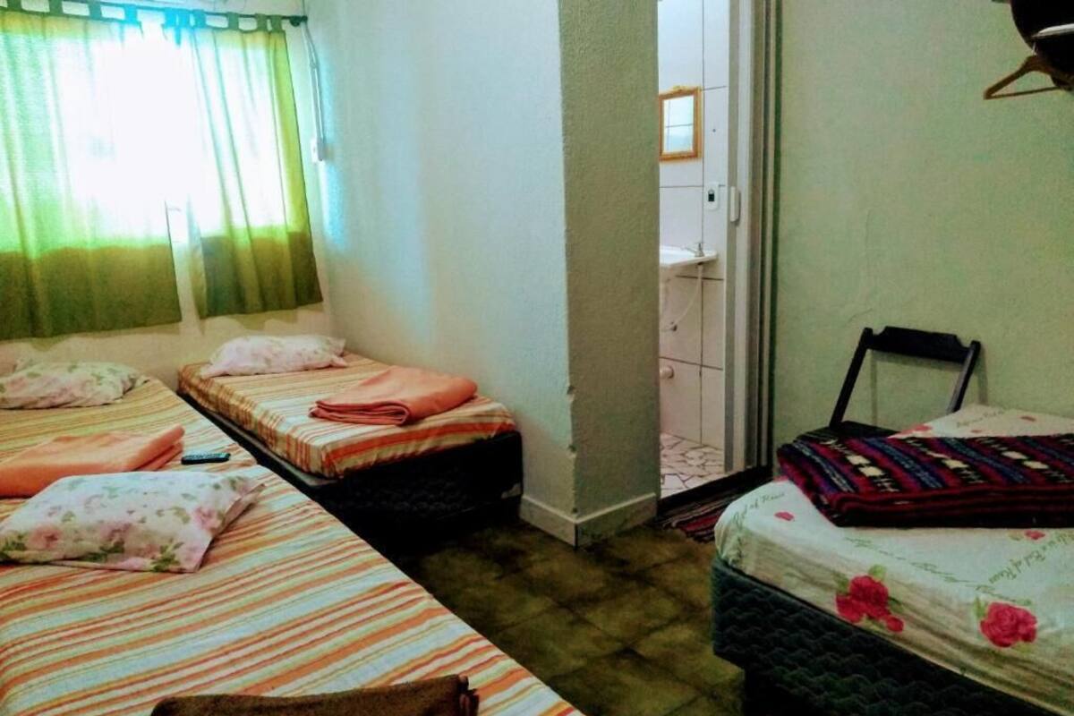 A room with three single beds, a small table, and a door leading to a bathroom.