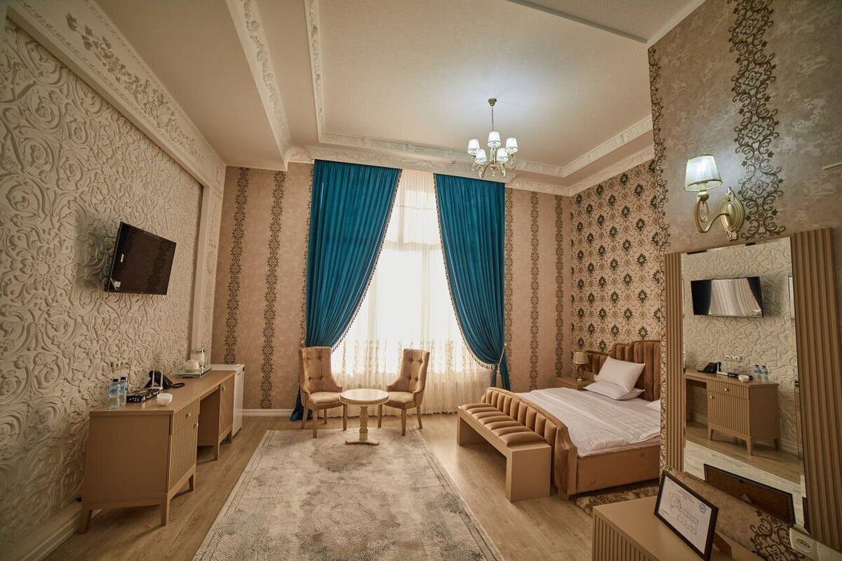 A hotel room with a bed, a desk, a chair, a sofa, a TV, a mirror, and a chandelier.