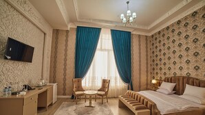 A hotel room with a bed, two armchairs, a small round table, a desk with a TV, and a nightstand with a lamp. - COMFORT HOTEL SAMARKAND (Samarkand)