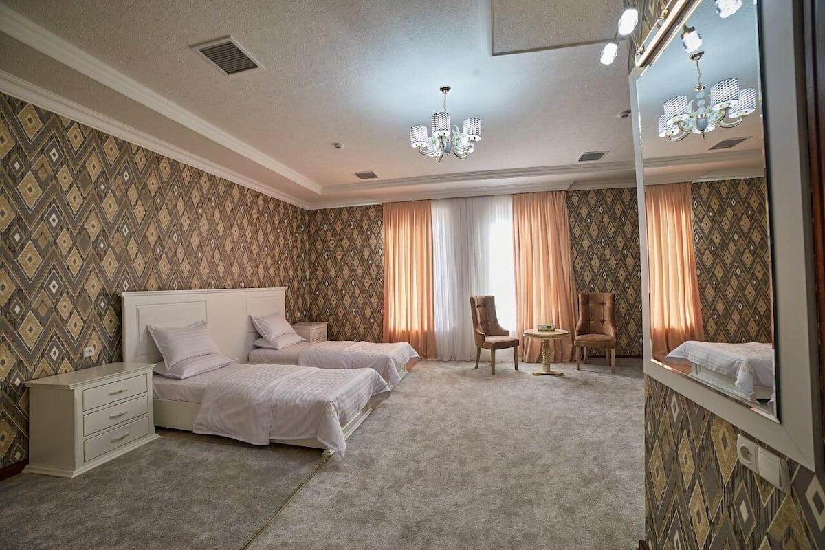A hotel room with two beds, a chair, a small table, and a mirror.