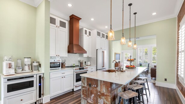 A modern kitchen with white cabinetry, a large island with stools, a built-in oven, and a stainless steel refrigerator.