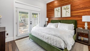 A bedroom with a green upholstered bed, white bedding, a wooden accent wall, and two framed botanical prints.