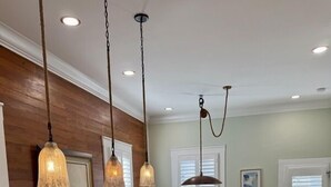 A kitchen with a marble countertop, wooden wall paneling, pendant lights, a fruit bowl, and a dining area with a table and chairs.