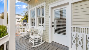 A porch with white rocking chairs and a small table, a door with a mailbox, and a white picket fence.