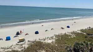 A beach with tents and beach chairs, a lifeguard tower, and a sandy shoreline. - Delightful Oceanview Studio (Myrtle Beach)