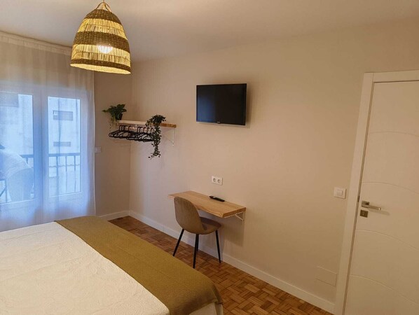 A bedroom with a bed, a desk, a chair, a television, and a hanging light fixture.