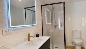A modern bathroom with a white vanity, a large mirror with LED lighting, a glass-enclosed shower, and a toilet. - Villa Galicia Padrón (Padron)