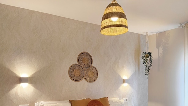A neatly made bed with a white and mustard-colored blanket, a wooden nightstand, and a wall-mounted light fixture. - Villa Galicia Padrón (Padron)