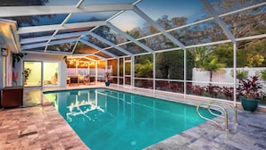A swimming pool with a glass enclosure, a covered seating area, and a view of the surrounding landscape.