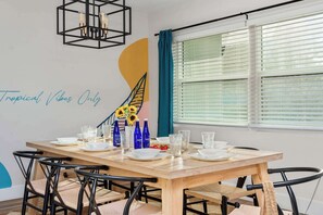 Un coin repas avec une table en bois dressée pour quatre personnes, des chaises noires et un luminaire suspendu moderne.