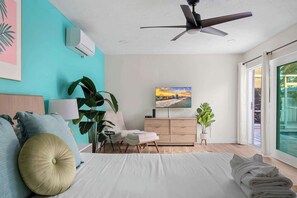 Une chambre à coucher moderne, équipée d’un lit, d’un ventilateur de plafond, d’une télévision, d’un bureau et d’une grande fenêtre.
