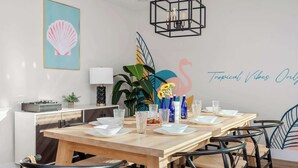 A dining area with a wooden table set for six, surrounded by black chairs. A large plant and a vase with sunflowers are on the table.
