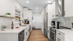 A modern kitchen with white cabinetry, stainless steel appliances, and a wooden floor.