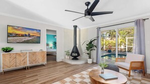 A modern living room with a large TV, a ceiling fan, a fireplace, and a view of a pool.