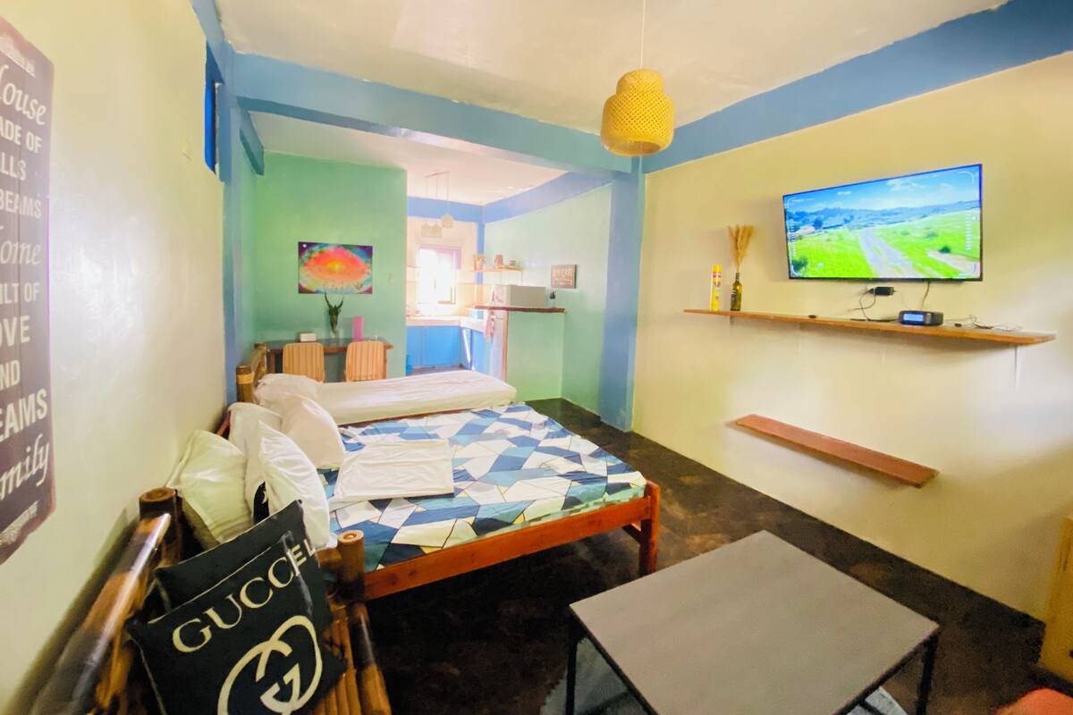 A hotel room with a bed, a small table, a TV on the wall, and a painting on the wall.