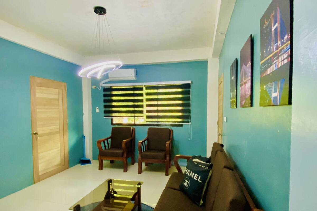 A living room with a blue wall, a wooden sofa, two armchairs, a coffee table, and a ceiling light fixture.