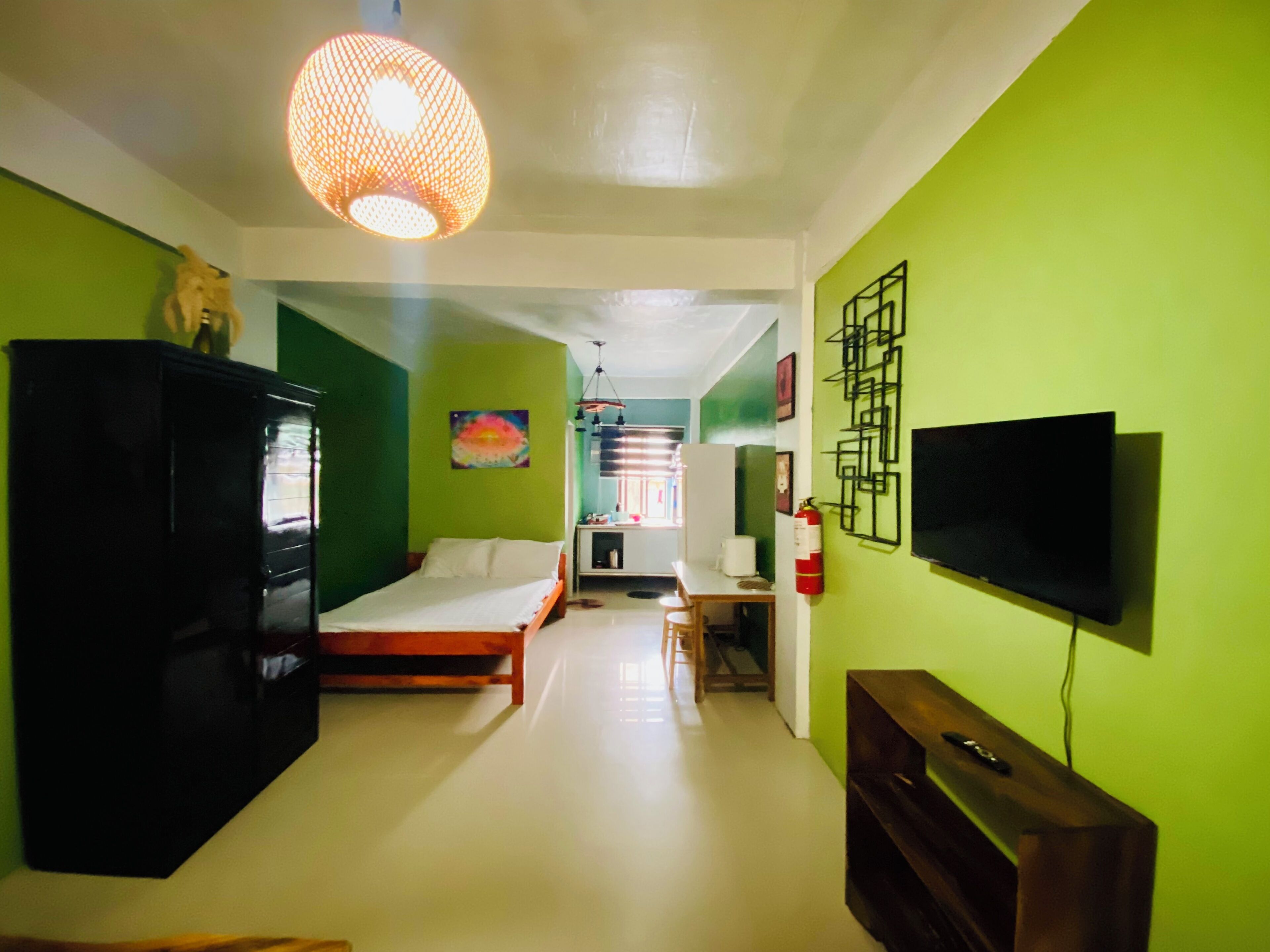 A room with a bed, a TV mounted on the wall, a cabinet, and a hanging light fixture.