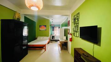 A room with a bed, a TV mounted on the wall, a cabinet, and a hanging light fixture.