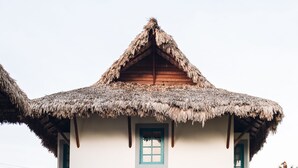 Una casa de dos pisos con techo de paja, paredes blancas y detalles azules.