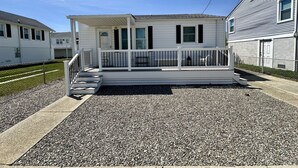 A single-story house with a front porch, a small deck, and a gravel driveway. - 2 bedroom, 1 bath, North Wildwood beach cottage! (North Wildwood)