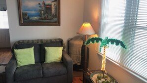 A living room with a grey sofa, a painting of a coastal scene, a lamp, and a decorative plant. - 2 bedroom, 1 bath, North Wildwood beach cottage! (North Wildwood)