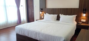 A hotel room with a large bed, two bedside tables with lamps, a wooden headboard, and a window with curtains. - Hotel Aerolink (Kathmandu)