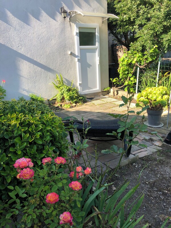 Relax in a serene garden setting with a wicker chair and lush greenery.