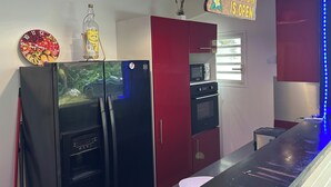A modern kitchen with a black refrigerator, a red cabinet, and a sign indicating a bar is open. - Studio, bas de Villa « La Marguerite » (Deshaies)